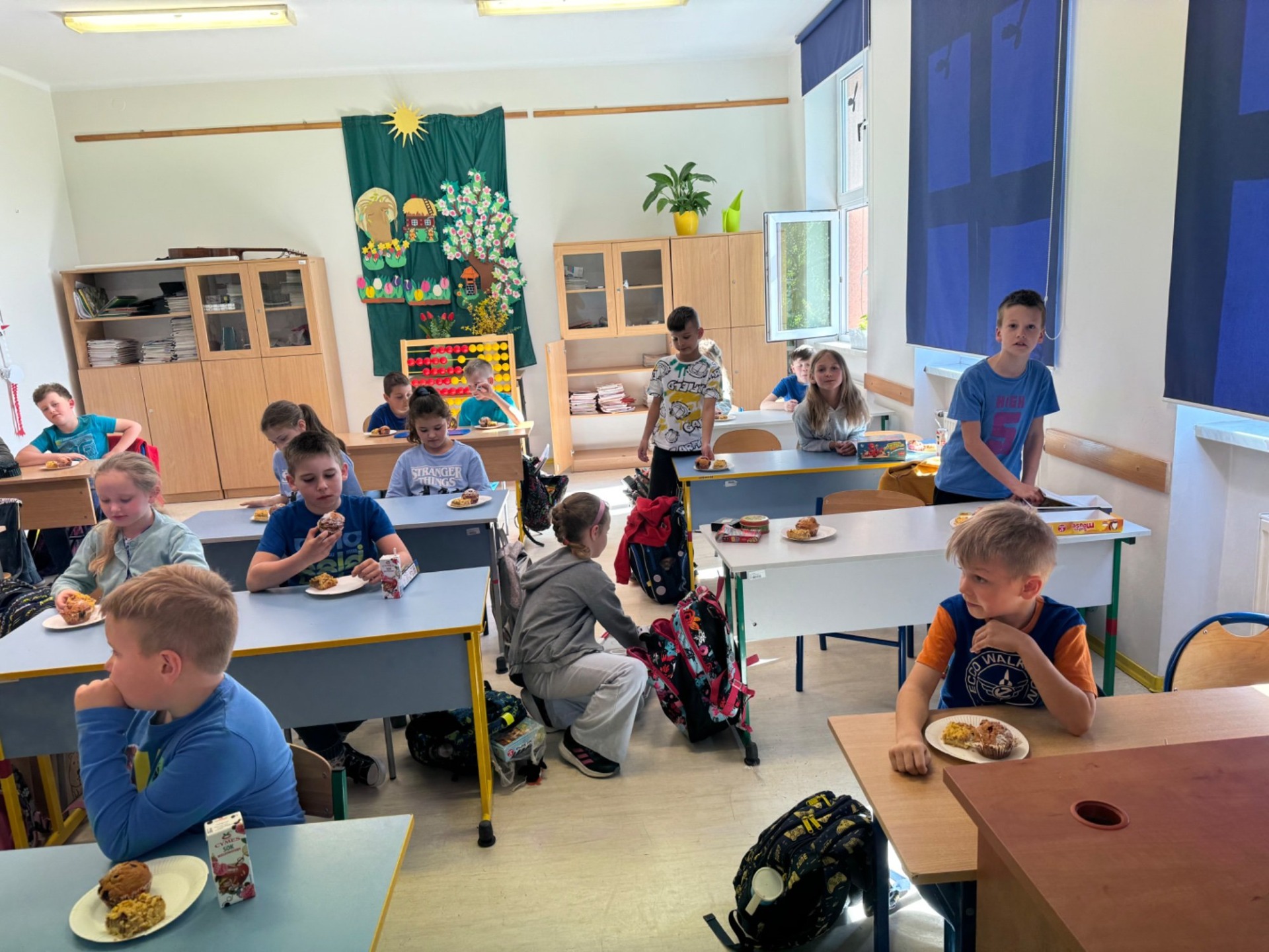 Uczniowie w ławkach jedzą słodkości z okazji 100 lekcji 