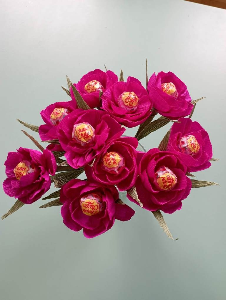 Drugie zdjęcie przedstawia bukiet złożony z dziewięciu kwiatów wykonanych z czerwonej bibuły. Środkiem kwiatów są czerwone lizaki Chupa Chups.