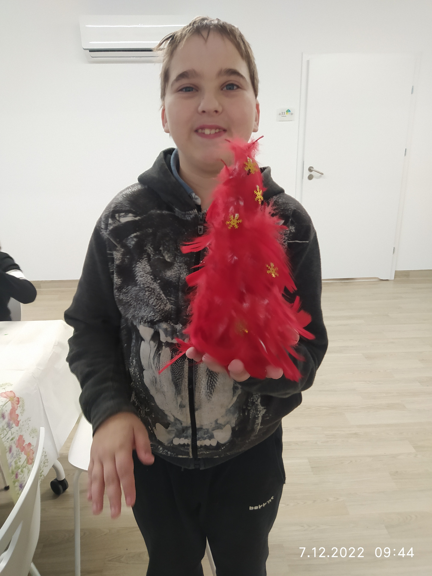 Chłopiec trzyma w rękach czerwoną choinkę z piórek