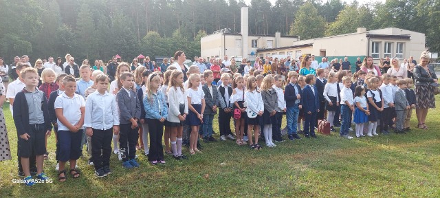 Grupa uczniów i rodziców stoi na boisku szkolnym. 