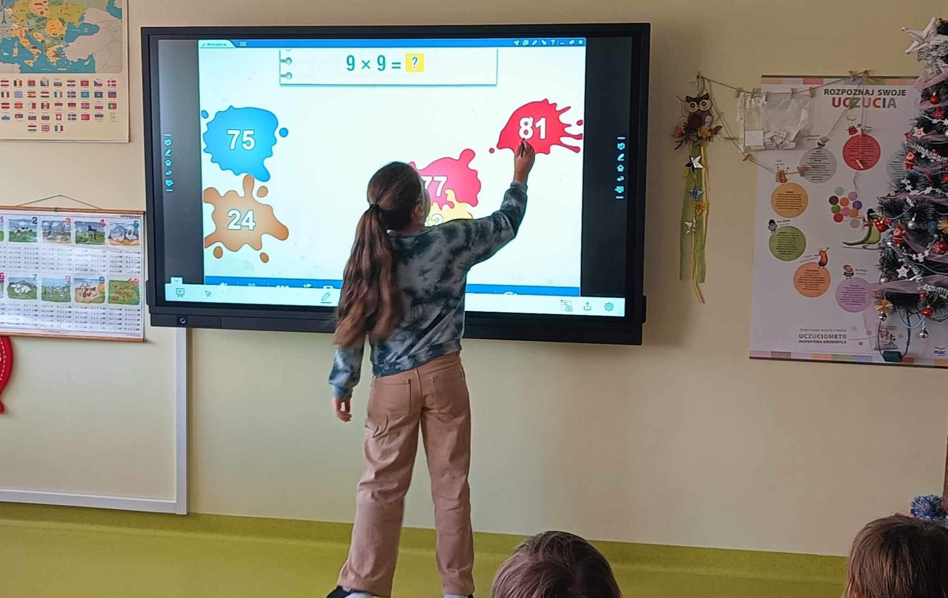 Uczniowie rozwiązują quizy matematyczne na monitorze interaktywnym.