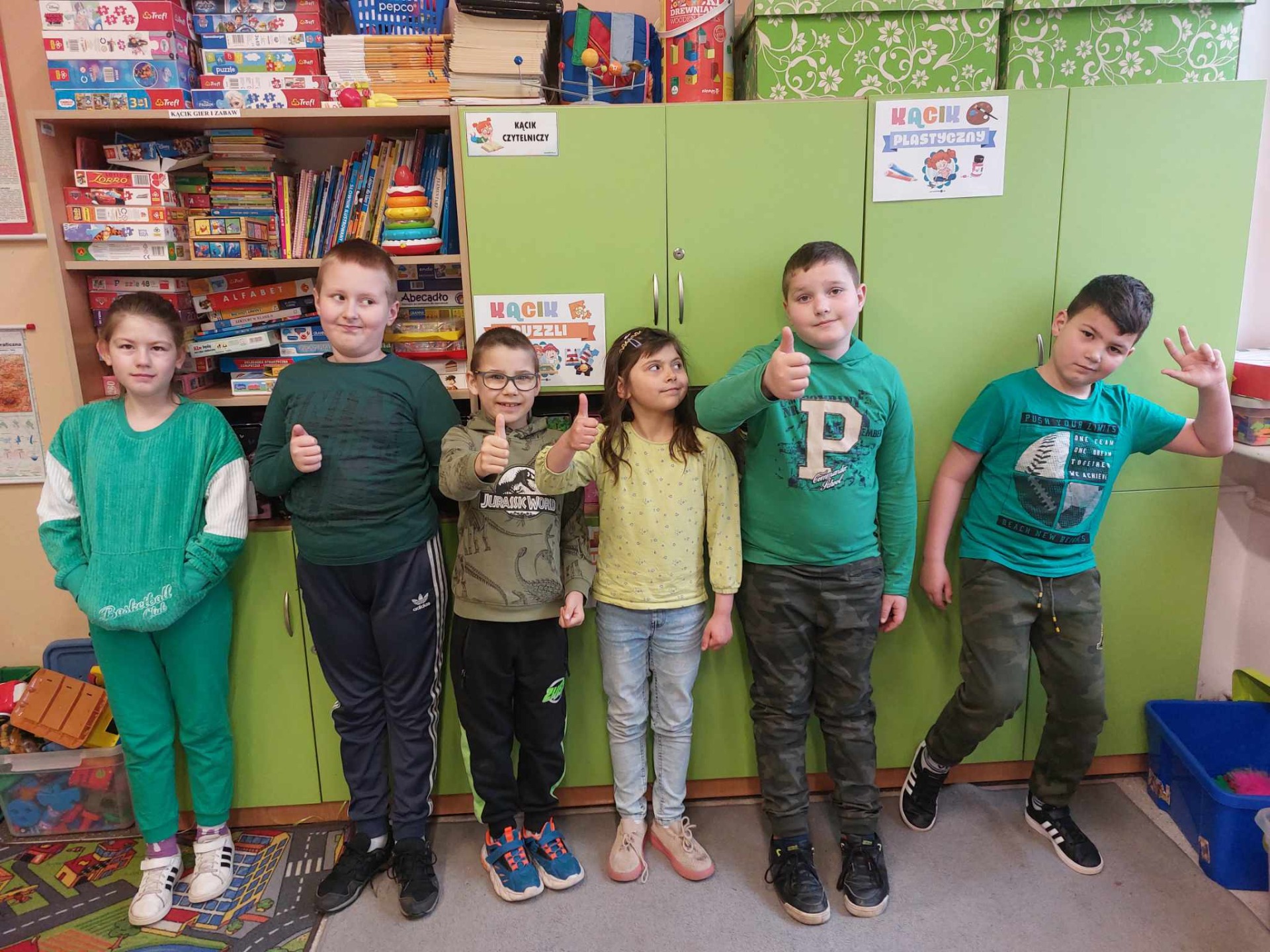 Grupa młodszych uczniów stoi i pozuje do zdjęcia, są ubrani na zielono