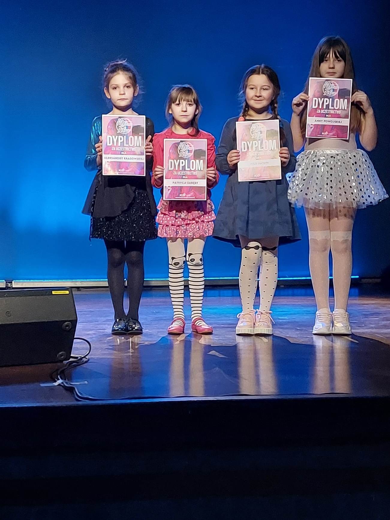 Cztery dziewczynki z dyplomami w ręku na scenie