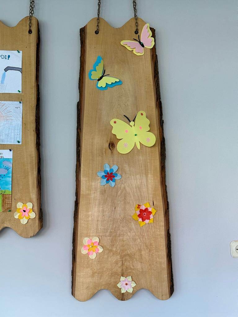 Zdjęcie piąte przedstawia dekorację świetlicy szkolnej. Na drewnianych deskach powieszone są kolorowe kwiaty i motyle.