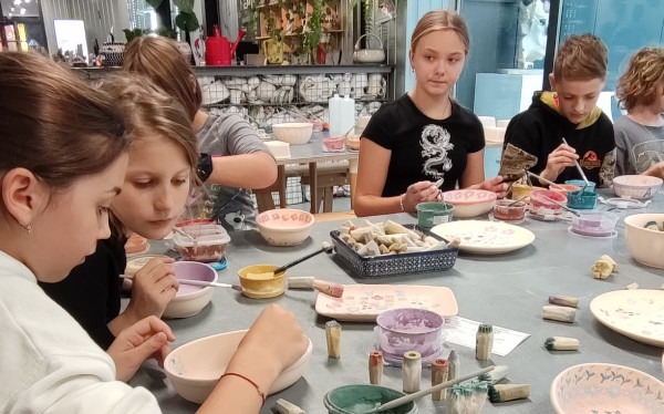 Warsztaty ceramiczne - kilka uczennic przy stole zdobi farbami miseczki