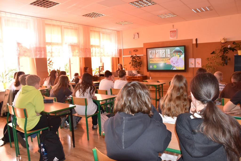 Uczniowie na spotkaniu z gośćmi z SANEPID-u oglądają prezentację multimedialną wyświetlaną na monitorze interaktywnym.