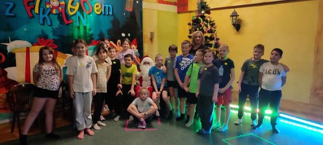 Grupa dzieci wraz z nauczycielką stoi przy Mikołaju i choince
