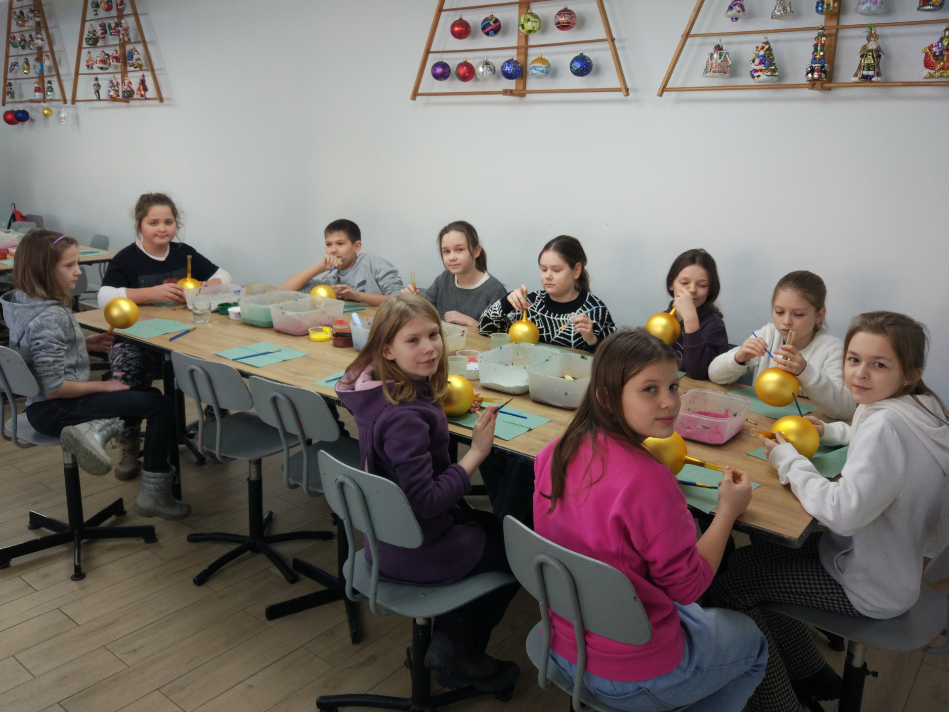 Na zdjęciu uczniowie klas 4 siedzą przy stole kolorując pędzlami bombki.