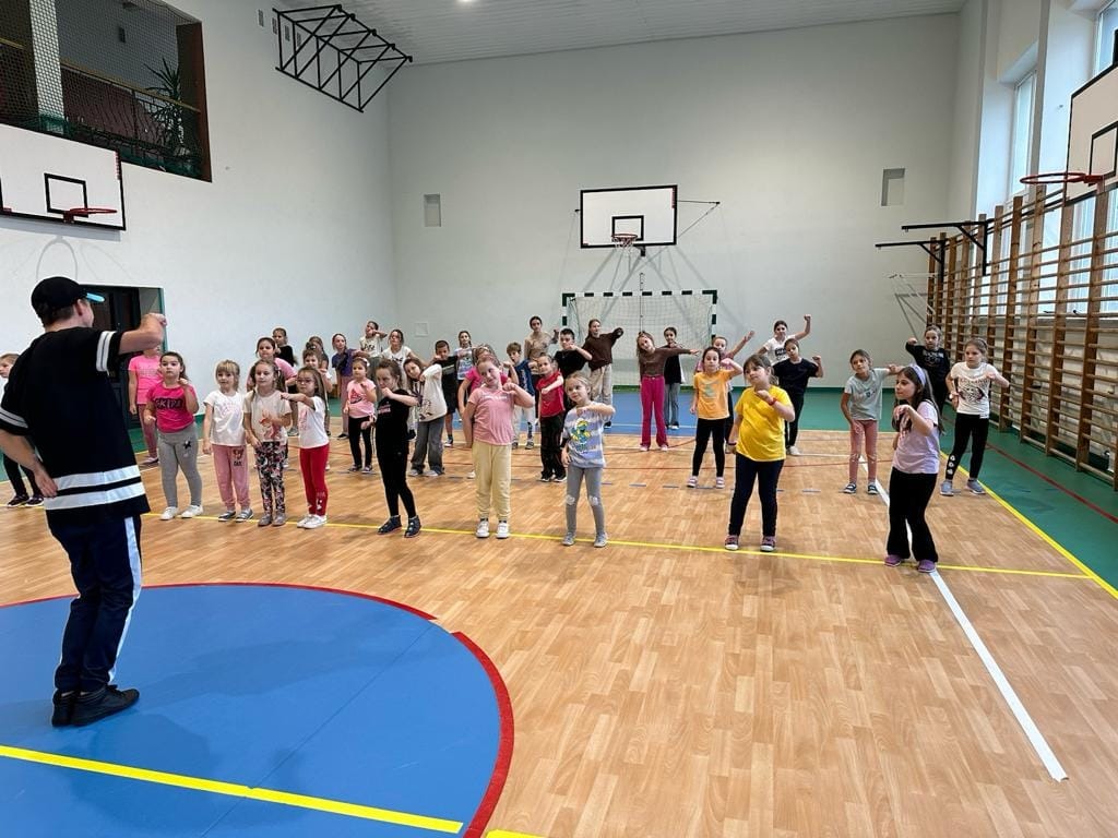 Na zdjęciu uczniowie należący do zespołu tanecznego „Frajda” wraz z instruktorem. Uczniowie wraz z instruktorem ćwiczą układy taneczne.
